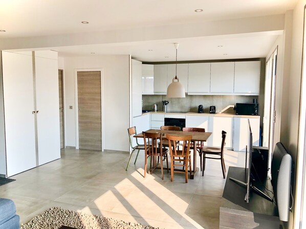 A modern kitchen with white cabinets, a dining area with wooden chairs, and a large pendant light.
