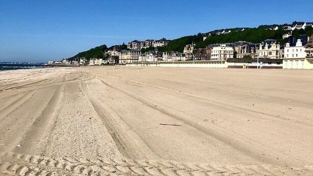 A wide sandy beach with visible tire tracks, a clear blue sky, and a hillside with buildings in the background. - TROUVILLE 3 Bdrms 65m2 SPLENDID AND CLEAR VIEW, BATHED IN LIGHT (Trouville-sur-Mer)