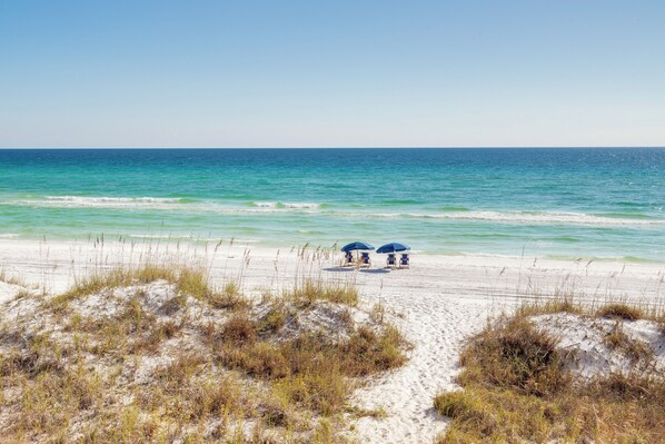 A beach with two blue umbrellas and a sandy path leading to the water.