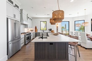 A modern kitchen with stainless steel appliances, a large island, and wicker pendant lights.