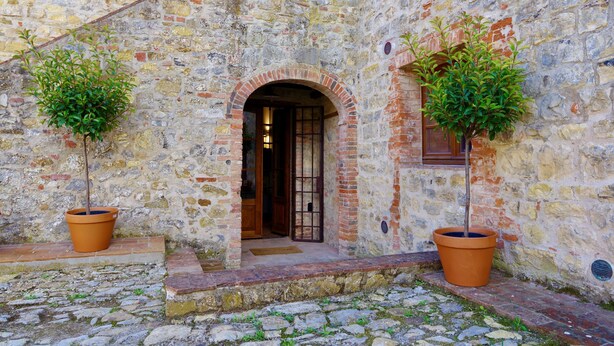 A stone building with an arched doorway, potted plants, and a cobblestone ground. - Serena al Casalone, Design apartment in Private Chianti Estate, pool WIFI A/C (San Gusme)