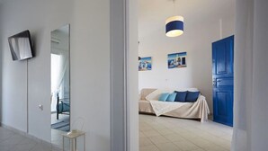 A modern hotel room with a large bed, a bedside table, a mirror, and a blue door. - Rodothea on the Beach. (Monolithos)