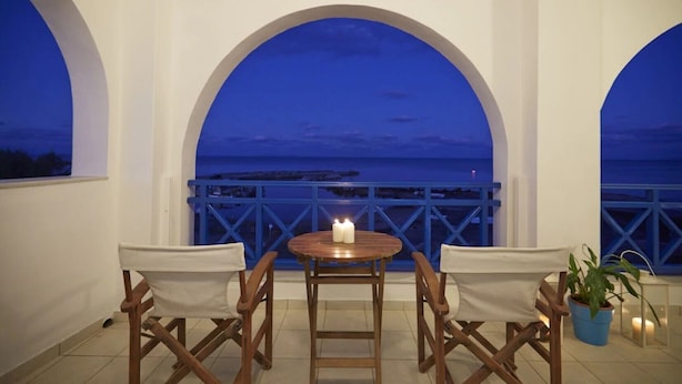 A balcony with a table and chairs, overlooking a coastal view at dusk. - Rodothea on the Beach. (Monolithos)