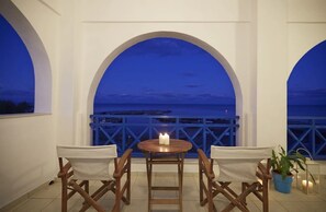 A balcony with a table and chairs, overlooking a coastal view at dusk. - Rodothea on the Beach. (Monolithos)