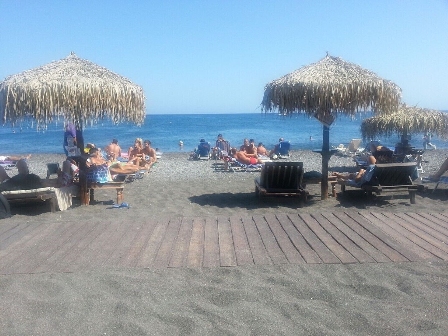 Ein Strand mit Holzliegen und Strohdächern, Menschen entspannen und sonnen sich.