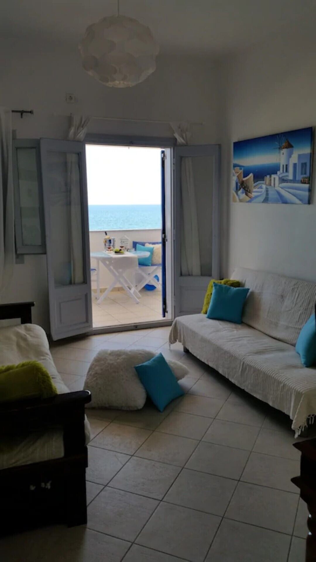 A room with a bed, a sofa, and a view of the sea through an open door.