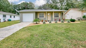 A single-story house with a front garage, a well-maintained lawn, and various small plants and shrubs in the front yard. - Fully Renovated Home in Downtown Clermont (Clermont)