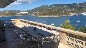A balcony with a table and chairs overlooking a bay with boats and hills in the background. - Amazing View, 3 Bed Renovated, AC, Generator (St Thomas)