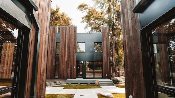 A modern building with a central entrance, wooden vertical elements, and a paved pathway leading to the entrance. - Pet-friendly, Cozy Tiny Home with Self Check-In and Wifi! (Spokane)
