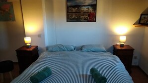 A neatly made bed with striped bedding and two rolled towels, two bedside lamps, and a framed picture on the wall.