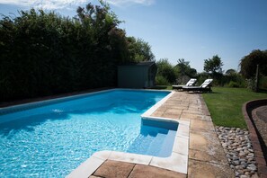 A swimming pool with a stone deck, two lounge chairs, and a small shed in a backyard. - Luxury Country Cottage with Access to Swimming Pool (High Halden)