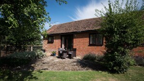 A brick house with a tiled roof, a front door, and a small patio area with a table and chairs. - Luxury Country Cottage with Access to Swimming Pool (High Halden)