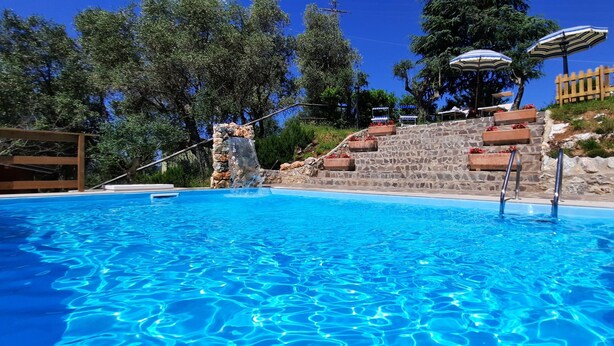 A swimming pool with clear blue water, stone steps, and outdoor umbrellas. - Mild hills Villa, on the Tuscany coast with brand new panoramic private pool (Camaiore)
