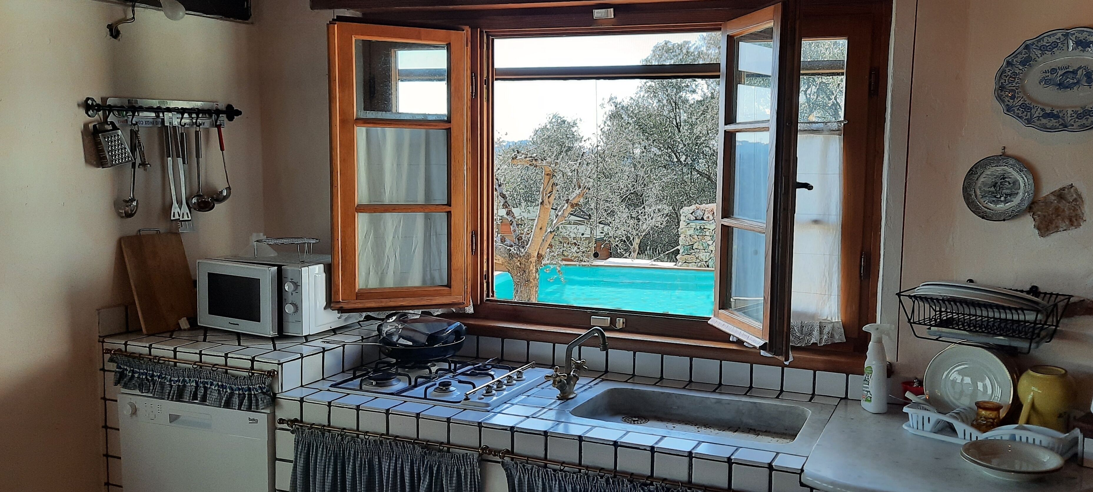 A kitchen with a gas stove, a microwave, and a window with an open door.
