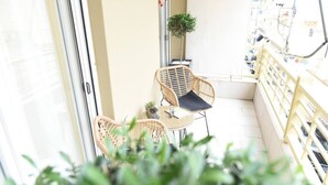 Ein Balkon mit Korbstühlen, einem kleinen Tisch, einer Topfpflanze und einem Geländer.