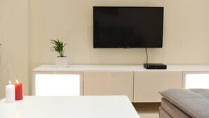 Ein modernes Wohnzimmer mit einem an der Wand montierten Flachbildfernseher, einem weißen Konsolentisch, einer Topfpflanze und einer Kerze.