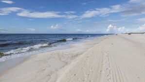 A wide sandy beach with gentle waves, a clear sky, and distant buildings. - NEWLY RENOVATED CONDO- ON BEACH (Orange Beach)
