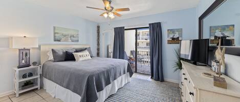 Un dormitorio con cama, ventilador de techo, televisor, cómoda y vistas al balcón.