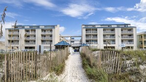 A pathway leading to a beachfront hotel with multiple balconies and a sandy beach in the background. - NEWLY RENOVATED CONDO- ON BEACH (Orange Beach)