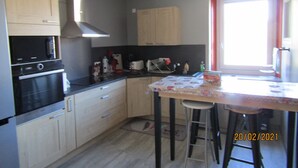 A compact kitchen with a microwave, stove, and sink. There is a small dining area with a table and two stools. The kitchen has wooden cabinets and a window with a red frame. - Gîte for 10 people (Prémanon)