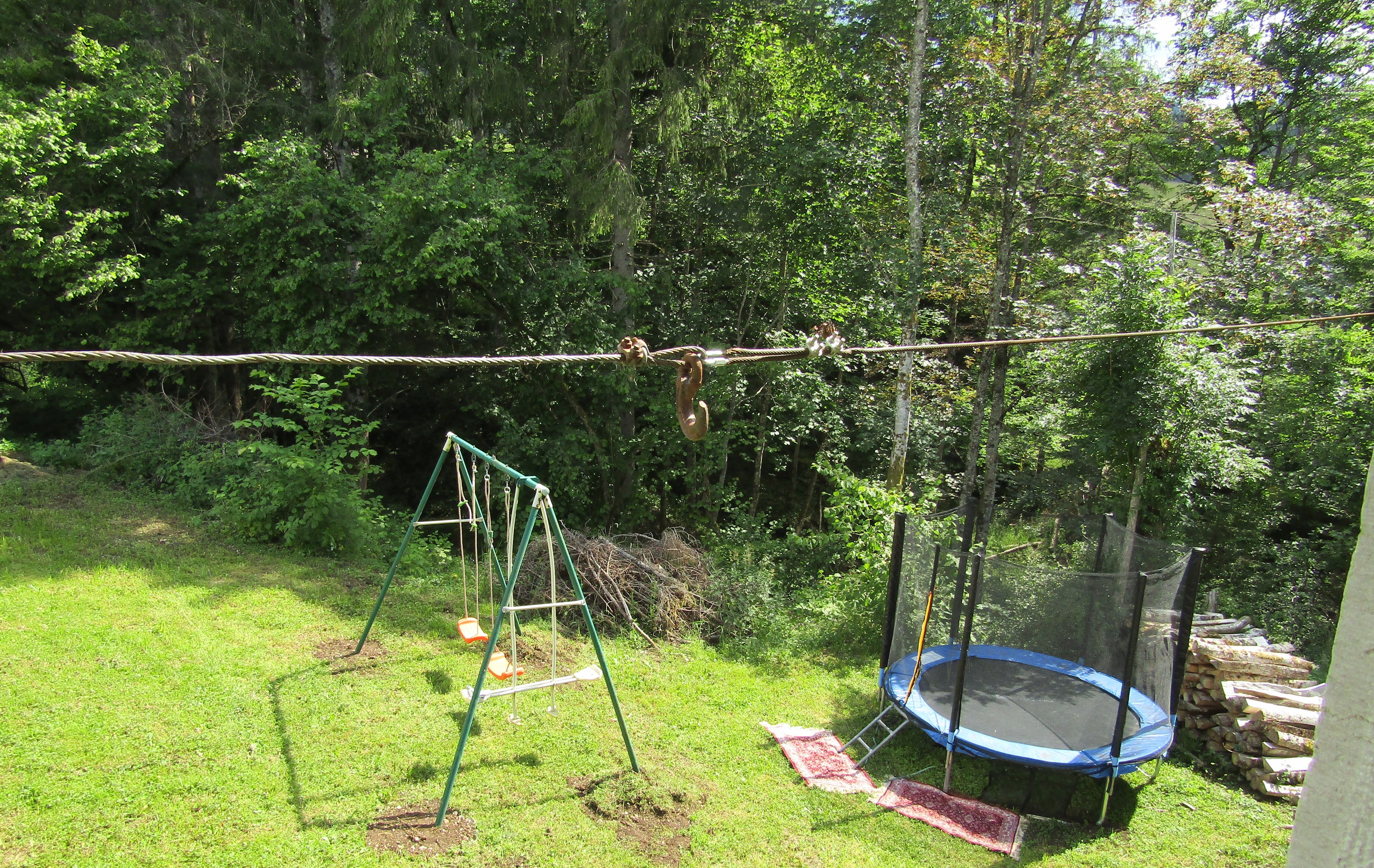 Un jardin avec une balançoire, un trampoline et une corde pour se balancer.