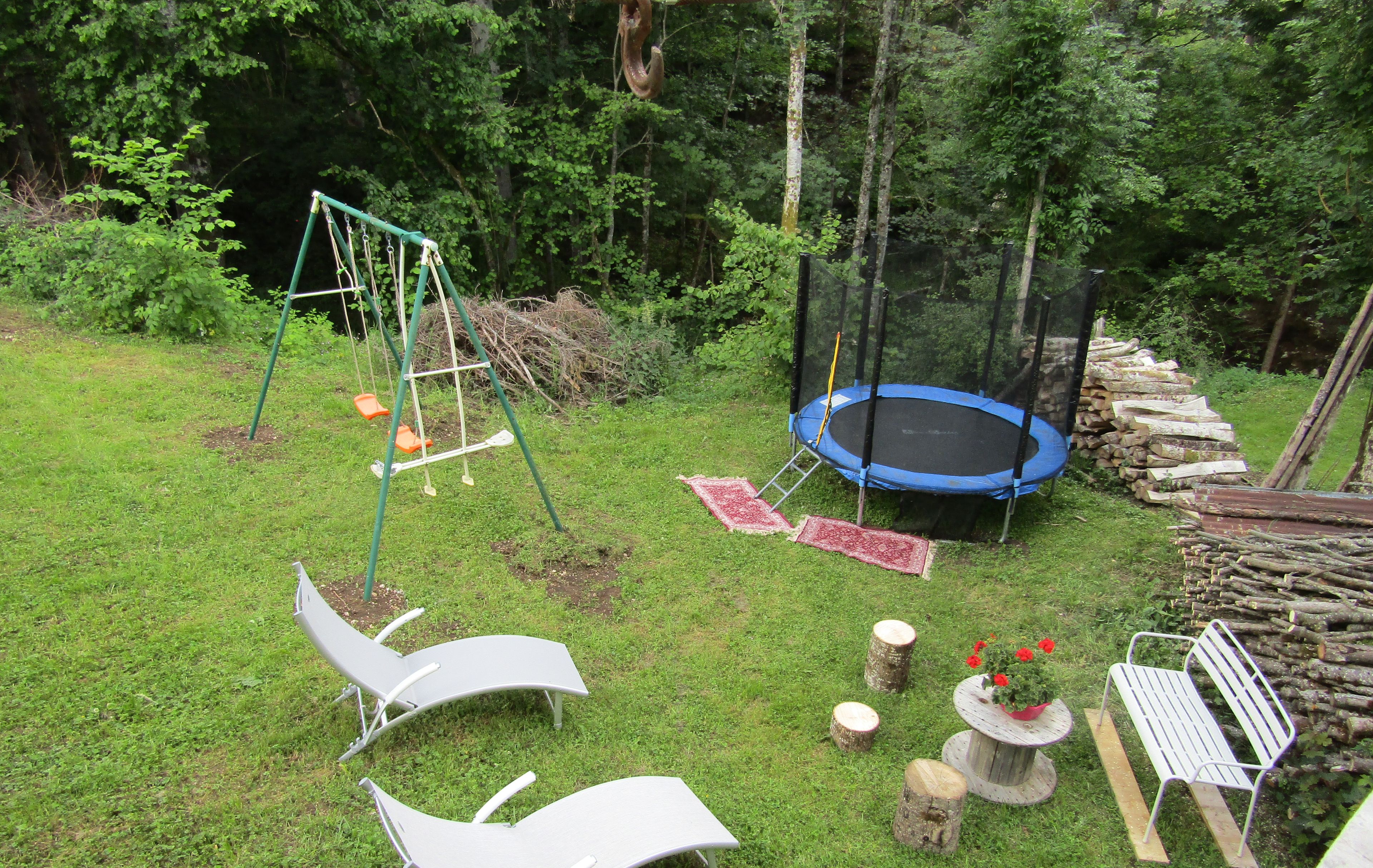 Ein Garten mit Trampolin, Schaukel und zwei Liegestühlen.