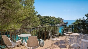 A terrace with wicker chairs and tables, overlooking a coastal landscape with trees and a view of the sea. - Villa Sa Caleta (Cala Santanyí)