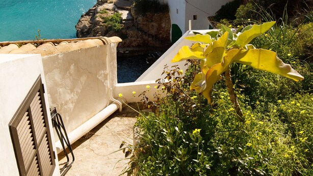 A coastal building with a staircase leading to a balcony overlooking the sea. - Villa Sa Caleta (Cala Santanyí)
