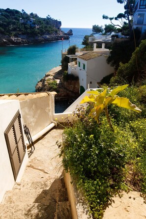 A coastal building with a staircase leading to a balcony overlooking the sea. - Villa Sa Caleta (Cala Santanyí)