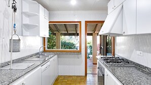 A compact kitchen with white cabinets, a granite countertop, and a window providing a view of greenery outside. - Villa Sa Caleta (Cala Santanyí)