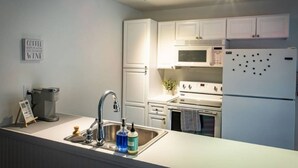 Una cocina moderna con gabinetes blancos, un lavamanos de acero inoxidable, un microondas, un horno y un refrigerador.