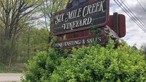Letrero de Six Mile Creek Vineyard con un mensaje de bienvenida, menciones de degustación de vinos y un saludo.