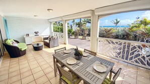 Un patio techado al aire libre con una mesa de comedor para dos, rodeado de mobiliario de mimbre y vistas al océano.