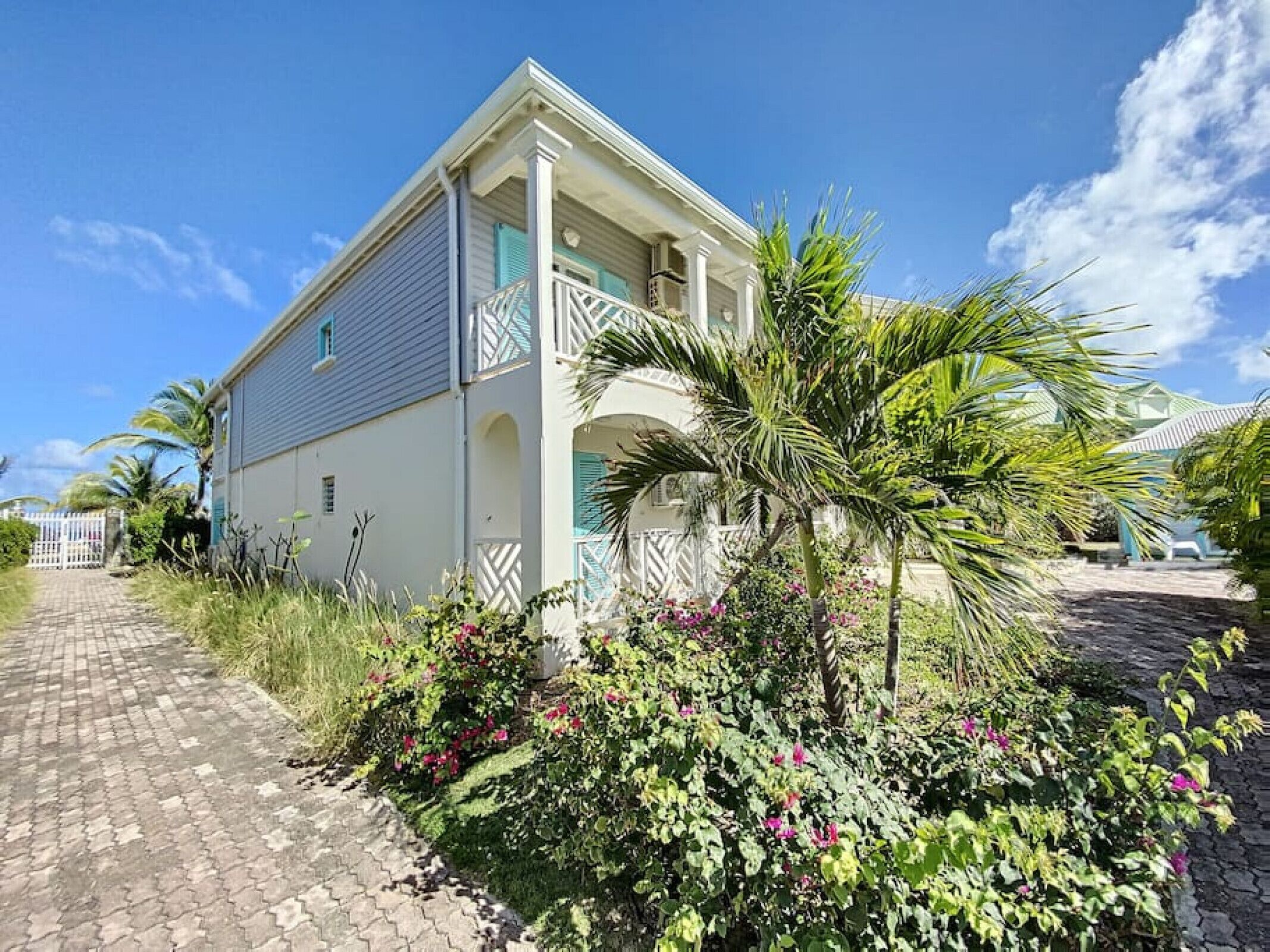 A two-story house with a balcony, surrounded by lush greenery and a paved pathway.