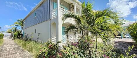 A two-story house with a balcony, surrounded by lush greenery and a paved pathway.