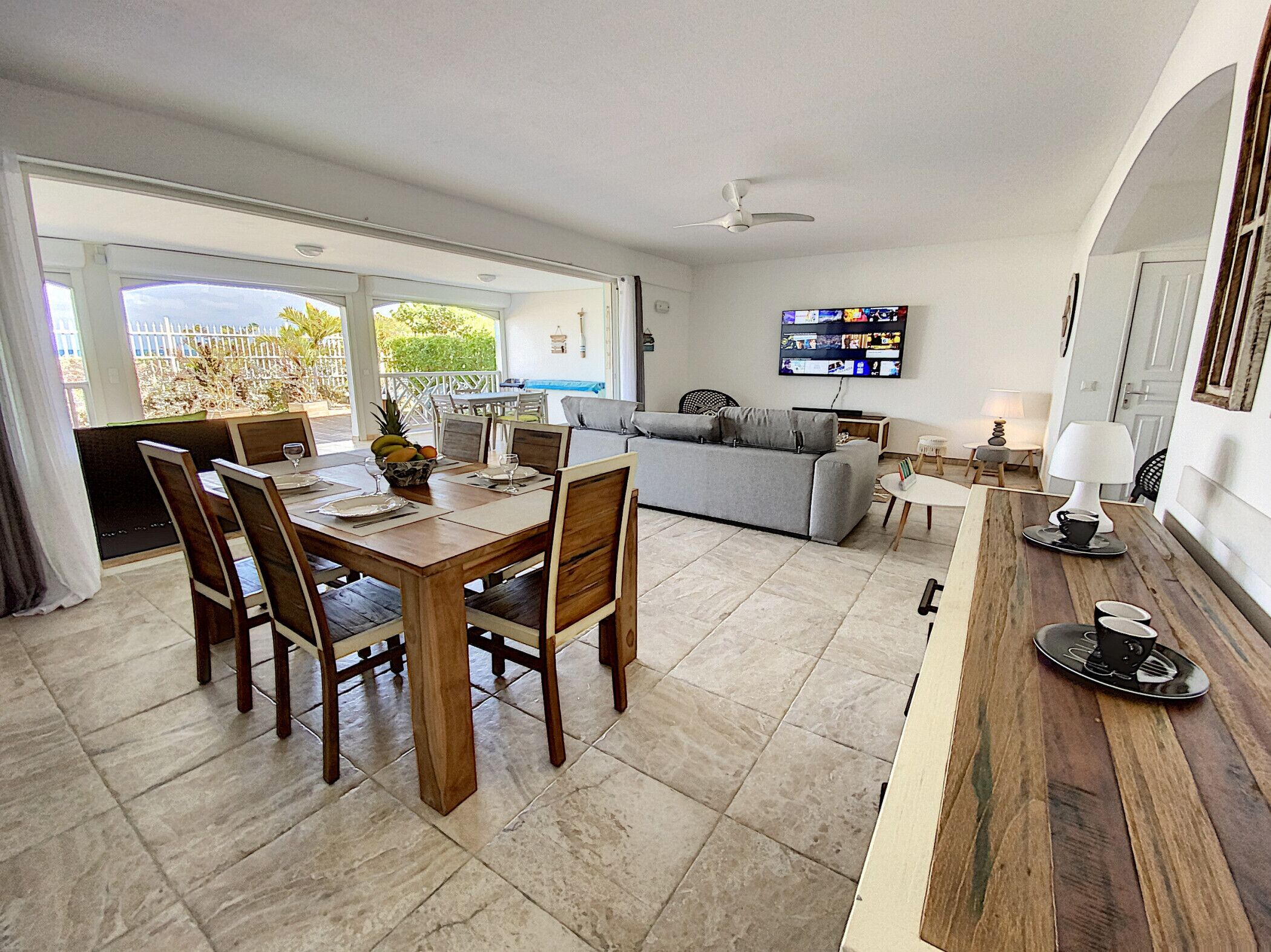 A spacious living area with a dining table, chairs, a sofa, and a TV mounted on the wall.