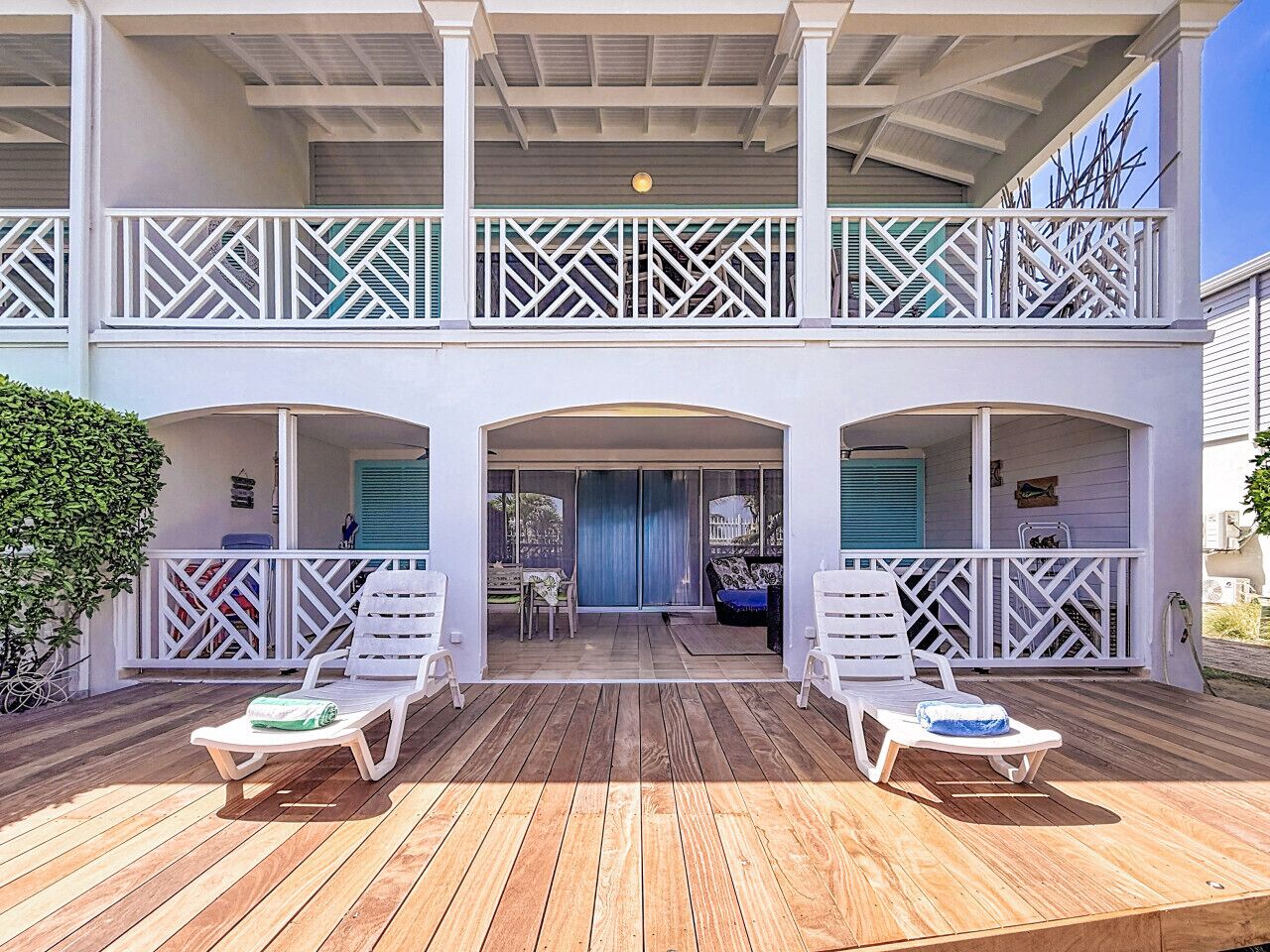 A two-story building with a wooden deck, white railings, and a covered area with lounge chairs.