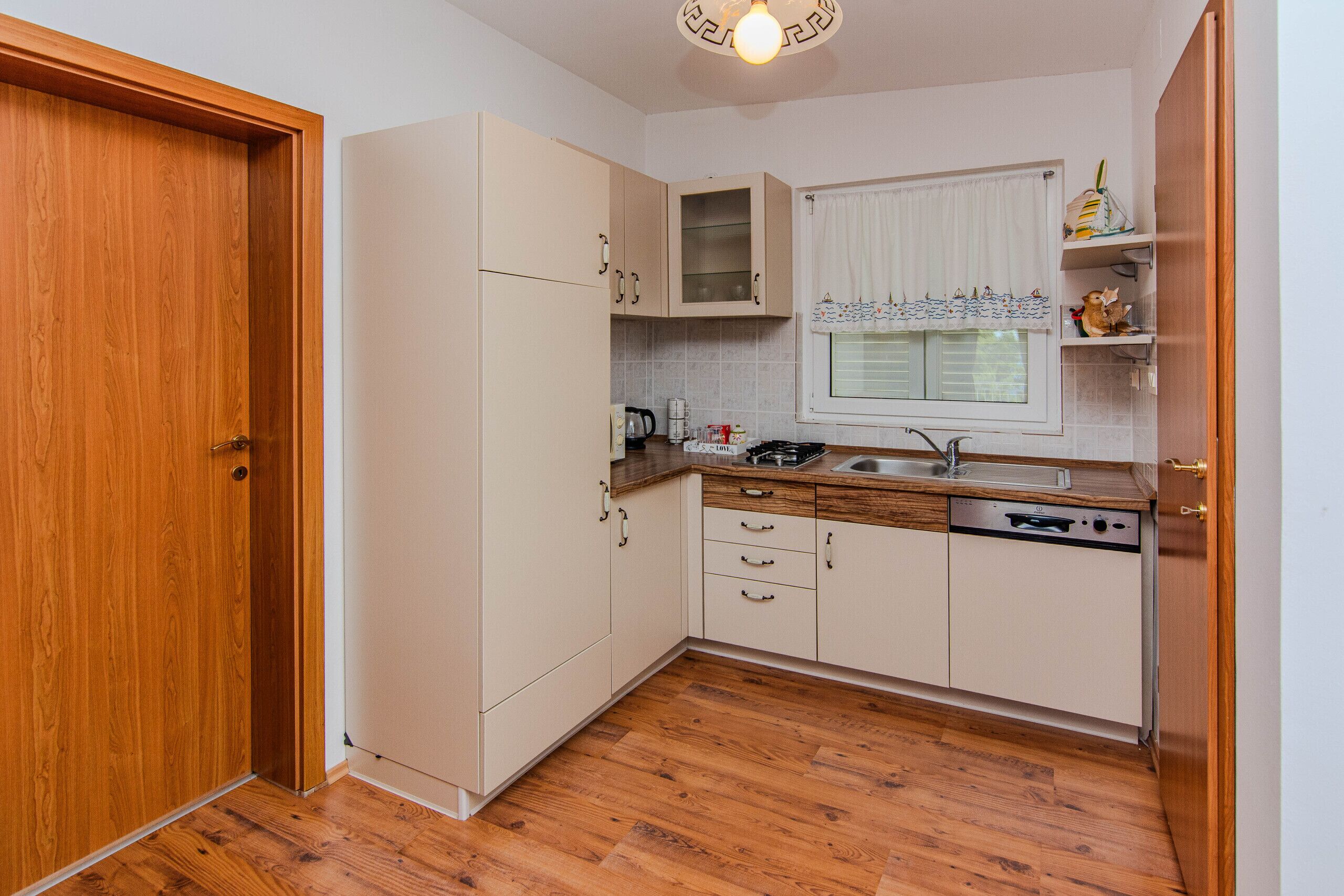 Una cucina compatta con mobili in legno, forno integrato e finestra con tende.