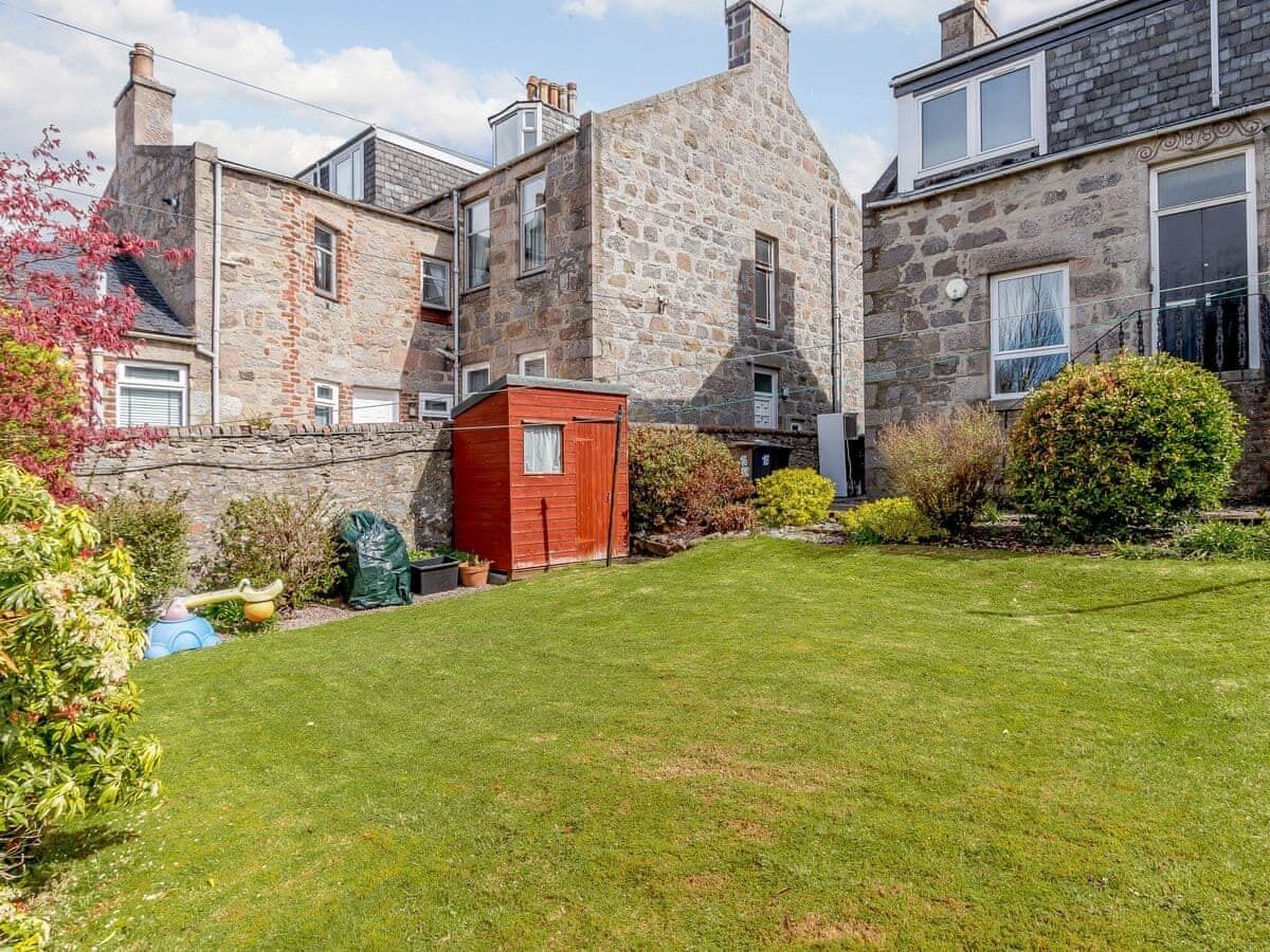 A stone building with a red shed in the yard, surrounded by well-maintained grass and shrubs.