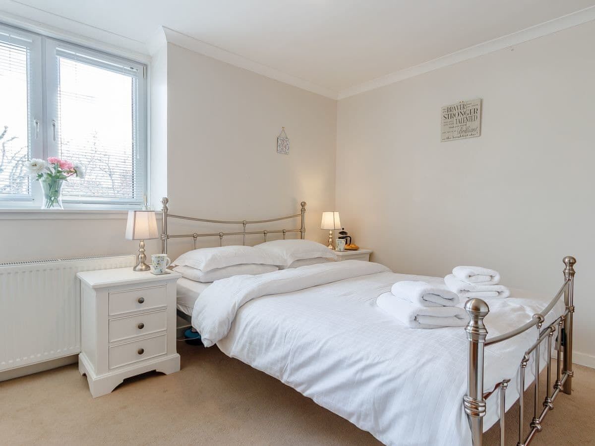 Un dormitorio ordenado con cama, mesitas de noche y una ventana con persianas.