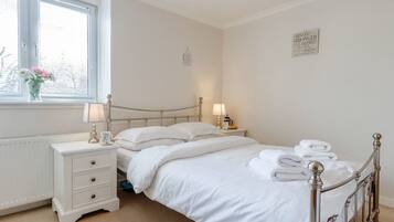 Un dormitorio ordenado con cama, mesitas de noche y una ventana con persianas.