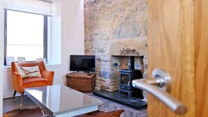 A room with a stone wall, a fireplace, a television, a cushioned chair, and a wooden door. - Ben Shea Smart Home (Keith)