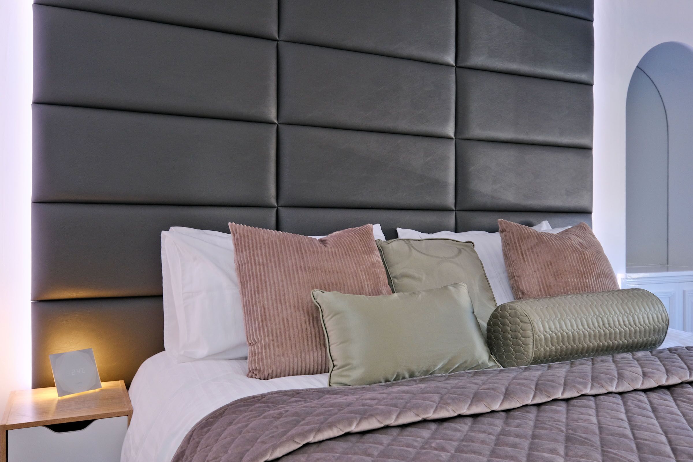 A bed with a dark headboard, multiple pillows, and a bedside table with a lamp.