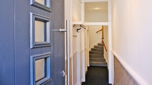 A narrow hallway with a door, a staircase, and a coat rack. - Ben Shea Smart Home (Keith)