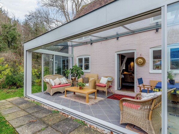 A modern house with a glass-enclosed patio, wicker furniture, and a garden view.