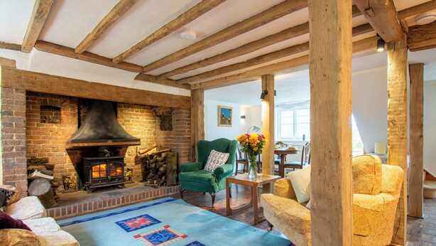 A cozy living room with exposed wooden beams, a brick fireplace, and a patterned rug. - 4 bedroom accommodation in Dallington, near Heathfield (Dallington, near Heathfield)