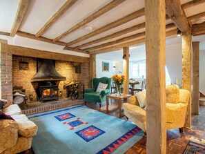 Ein gemütliches Wohnzimmer mit freiliegenden Holzbalken, einem Kamin aus Backsteinen und einem gemusterten Teppich.