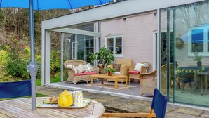 A modern outdoor patio with wicker furniture, a table with a yellow teapot, and a glass door leading to a room. - 4 bedroom accommodation in Dallington, near Heathfield (Dallington, near Heathfield)