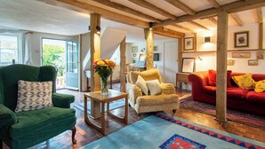 A room with a green armchair, a red sofa, wooden beams, a wooden table with a vase, and a patterned rug. - 4 bedroom accommodation in Dallington, near Heathfield (Dallington, near Heathfield)