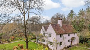 A pink house with a sloped roof, surrounded by a grassy yard and trees. - 4 bedroom accommodation in Dallington, near Heathfield (Dallington, near Heathfield)